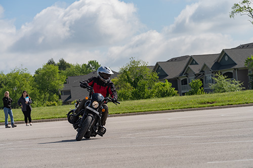 A person wearing a helmet, driving a motorcycle through a parking lot.